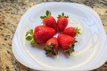 Juicy fresh strawberries in a dish white, on a marble table background, delicious dessert.