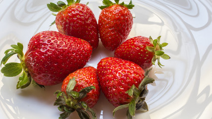 Juicy fresh strawberries in a dish white, on a marble table background, delicious dessert.