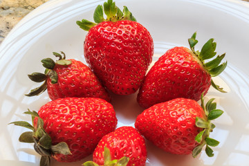 Juicy fresh strawberries in a dish white, on a marble table background, delicious dessert.