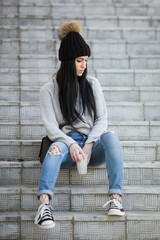 Fashionable woman sitting on stairs wearing ripped jeans with sneakers.