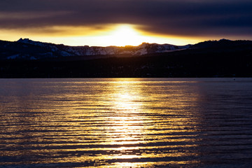 Bright sunset on the shoreline of Lake Tahoe, Sierra Mountains covered in snow visible in the...