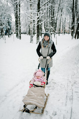 Fototapeta na wymiar A happy young mother with daughter, walks with baby and a children sled outdoors on the background winter. Close up. Happy family walking in the park. Infant.