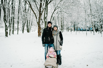 Mom, Dad and daughter stand outdoors on the background winter. Happy family walks in the park. full length. Close up. Portrait baby in children's sled. Infant.