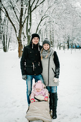 Mom, Dad and daughter stand outdoors on the background winter. Happy family walks in the park. full length. Close up. Portrait baby in children's sled. Infant.