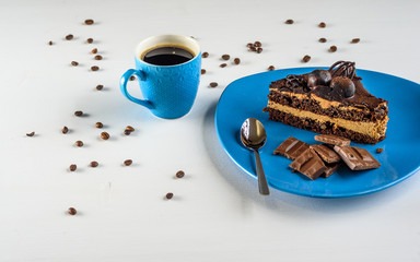 A piece of chocolate cake, and pieces of chocolate on a blue plate, next to a cup of coffee, on a light wooden background.