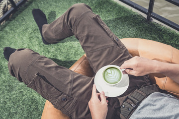 Enjoying fresh coffee. Man wearing cargo pants and holding cup while relaxing on couch at home