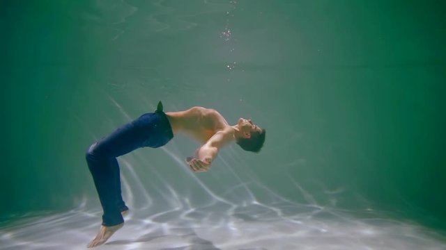Young muscular guy floating naked in the pool.