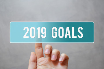 2019 goals - finger pressing blue transparent button on virtual touchscreen interface on gray background with copy space for text. New years resolutions and planning concept.