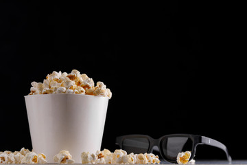 Snack to watch movies. Popcorn in a paper bucket and glasses on a dark background..