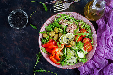 Fototapeta na wymiar Tuna salad with tomatoes, olives, cucumber, sweet pepper and arugula on rustic background . Top view