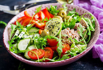Tuna salad with tomatoes, olives, cucumber, sweet pepper and arugula on rustic background