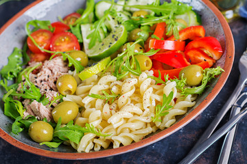 Buddha bowl. Pasta salad with tuna, tomatoes, olives, cucumber, sweet pepper and arugula on rustic background .