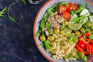 Buddha bowl. Pasta salad with tuna, tomatoes, olives, cucumber, sweet pepper and arugula on rustic background . Top view