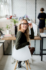 Portrait of cheerful blond woman, shop assistant, in office wear looking at camera while sitting at the table