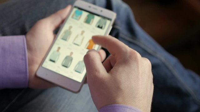 A man looks at the goods in the online clothing store. People using Smartphone, online shopping. The screen is blurred. Close-up. 4K UHD.