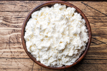 Homemade cottage cheese in a wooden bowl on old wooden table.