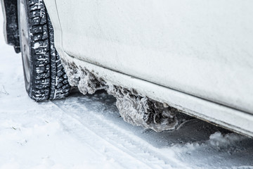 Detail view of frozen salt, snow and ice chunks stuck under car body, causes rust and corrosion in...