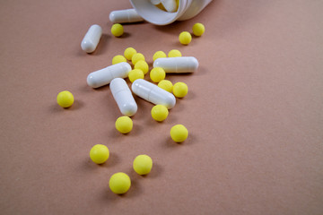 Mixed pills spilled out of the white bottle. Pharmaceutical medicine tablets, capsules and pills on the brown background