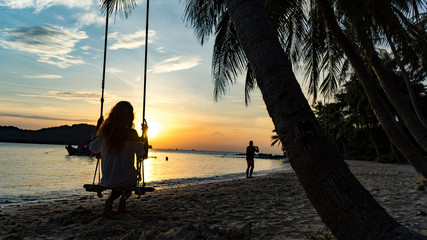 Silhouette of a girl whose sitting on a swing on the Phu Quoc island on the beautiful evening beach looking for sunset ,sea,boat and mountain