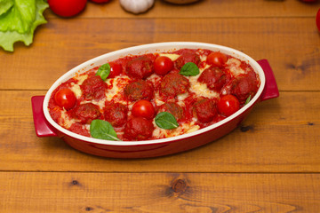 Meatballs in tomato sauce in a baking dish on a wooden table. Selective focus