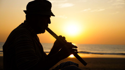 Silhouette of senior man playing bamboo flute on the beach at sunset © alexeg84