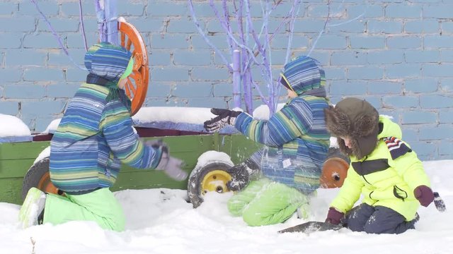 Funny children in warm colorful bright clothes playing with snow on background of pirate ship. kids love winter break. the boys are happy together