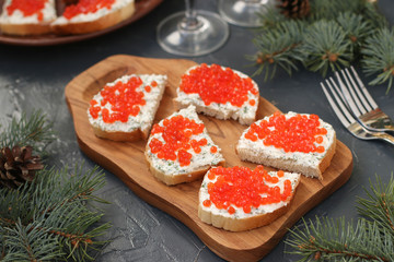 Sandwiches with red caviar are located on a wooden board against a dark background. Festive snack