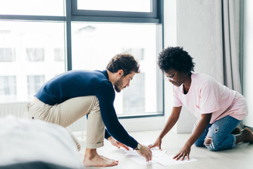 African and Caucasian mixed race married couple sitting on the floor at home checking unpaid bills, taxes, due debt, bank account balance. There is a time to gather the stones and a time to sum up.