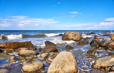 Big stones and waves under blue sky with clouds. Baltic Sea in Mecklenburg-Vorpommern.