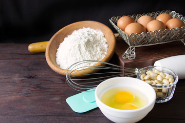 Items and ingredients for baking on a wooden background. Eggs, flour , nuts, rolling pin, wisk and paddle on brown wooden table