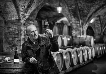 Mann bei Weinprobe mit Rotwein in Gewölbekeller, schwarzweiß