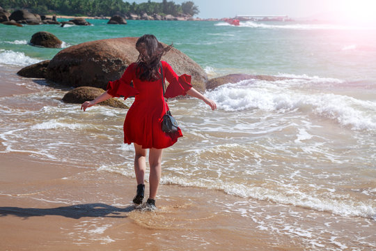 Beautiful woman walks at the sea side, happy girl in a red dress and shoes went into the sea;
