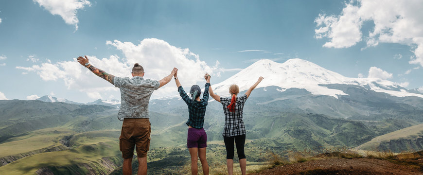 Three friends joined hands and raised their hands up, enjoying the view of the mountains in the summer. Lifestyle Travel Happy Emotions Success Concept Summer Vacations Outdoor
