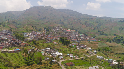 Fototapeta na wymiar asian town with mosque in mountains among agricultural land, rice terraces. mountains with farmlands, rice fields, village, fields with crops, trees. Aerial view farm lands on mountainside. tropical