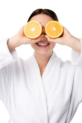 smiling woman in white bathrobe holding oranges in front of face isolated on white