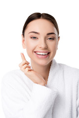 beautiful smiling woman in bathrobe with face cream on hand looking at camera isolated on white