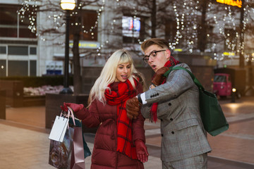 The surprising young couple standing in the street with shopping bags after good shopping and looking at the watch