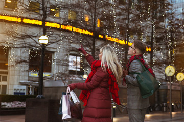 Fototapeta na wymiar The young couple standing in the street with shopping bags and looking at the big store