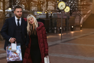 Portrait of the happy, elegant young couple who is standing on the street with shopping bags
