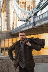 Portrait of the young man who is standing under the bridge and holding bag