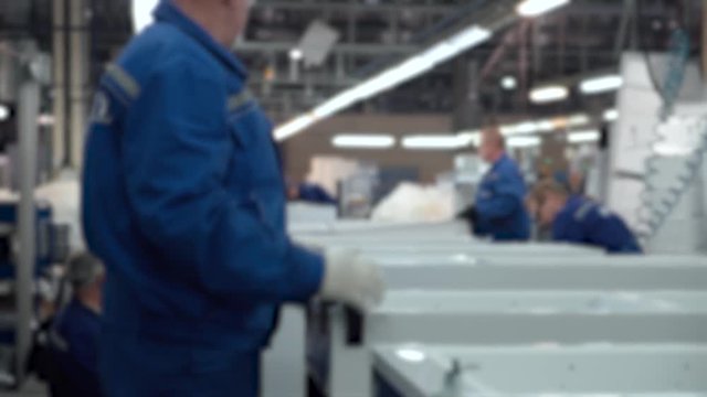 Blurred view of conveyor, masters and workers at work, part assembly process of element refrigerators, household appliances assembly shop.