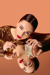 attractive woman in golden clothes with glamorous makeup, perfume bottle and mirror reflection...