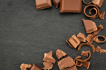 Broken chocolate pieces and chocolate shavings on a dark background. Top view with copyspace for your text