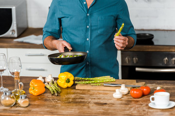 cropped image of middle aged man cooking vegetables on frying pan in kitchen