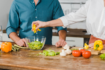 cropped image of mature wife and husband preparing salad together in kitchen