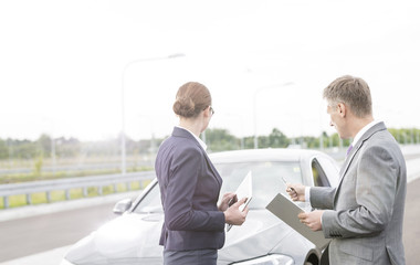 Insurance agent discussing with businesswoman while pointing at breakdown car against sky
