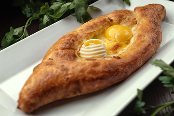 Adjar Khachapuri, an open pie with an egg, on a white plate. Traditional Georgian cuisine