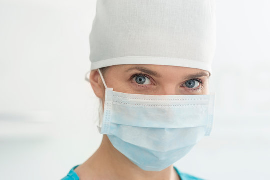 Closeup Portrait Of Female Doctor Wearing Surgical Mask And Cap At Clinic