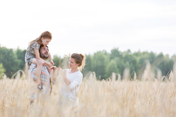 Happy family standing amidst wheat crops at farm against sky