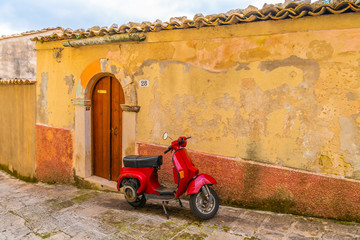 Red vintage motorbike Vespa on the street of italian ancient town Modica in Sicily, Italy